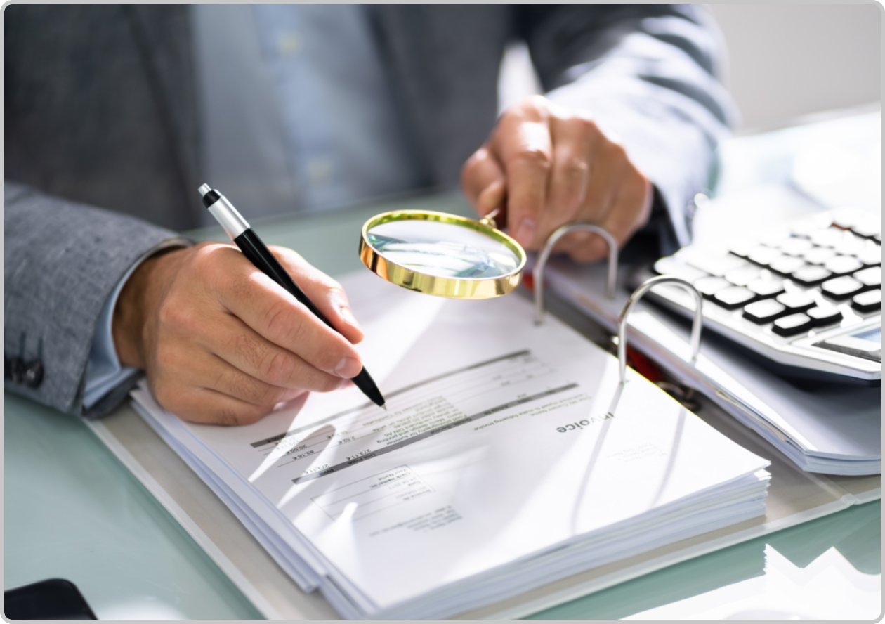 man in suit holding a gold magnifying glass and writing in a binder